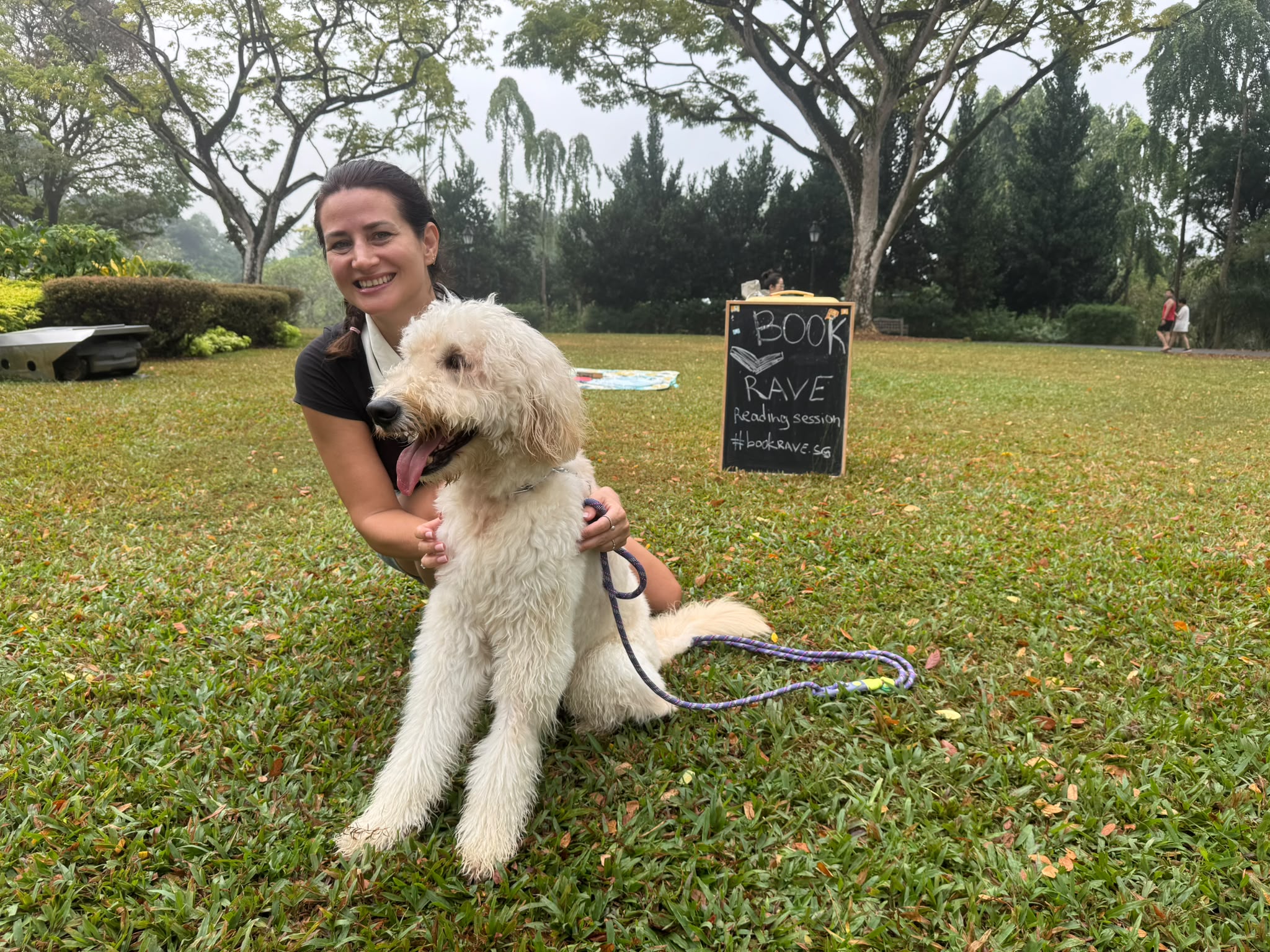 Anna with Ravi the dog beside the Book Rave sign on the lawn